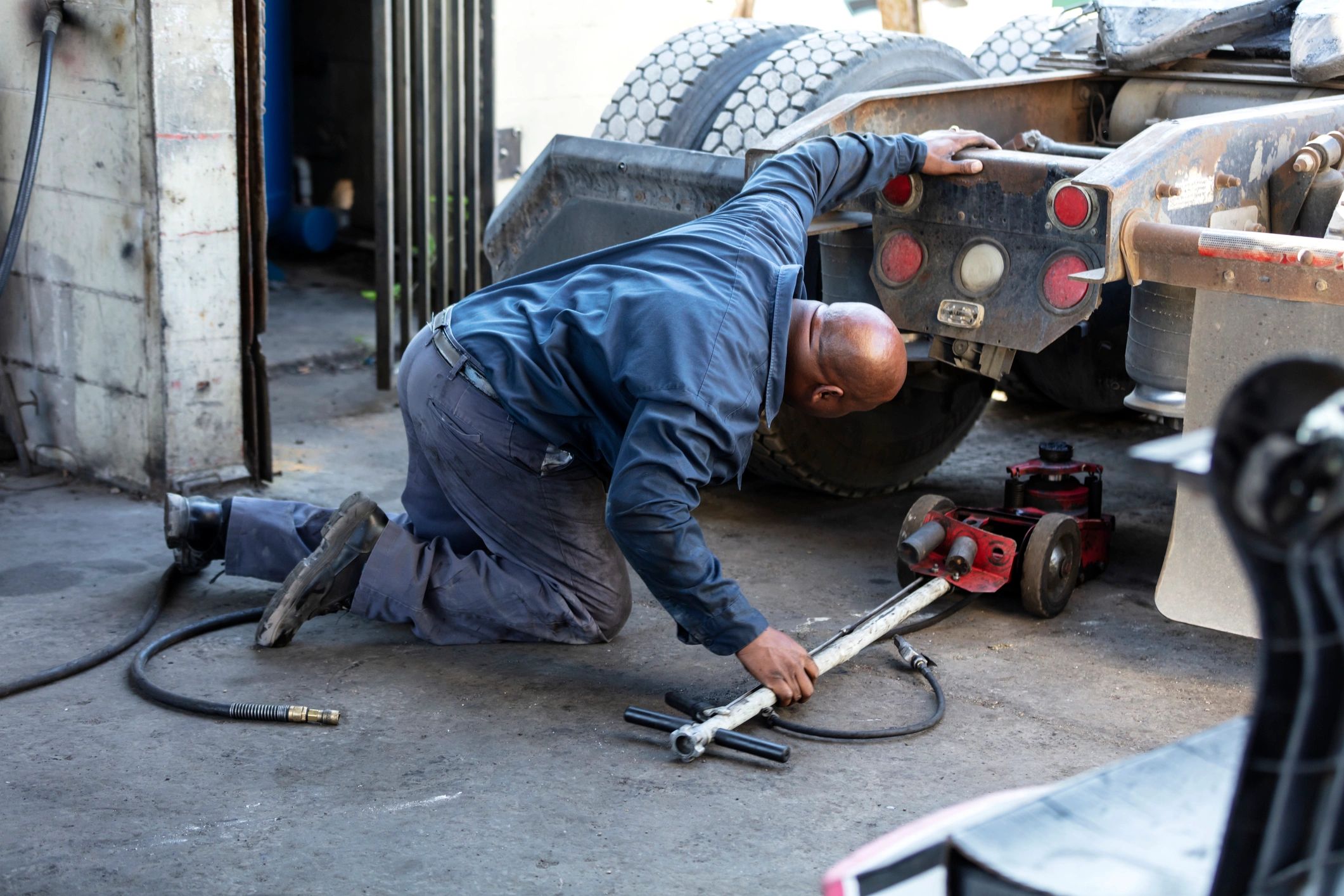 Mechanic inspecting the underside of a semi-truck in a repair shop